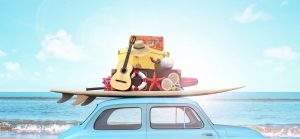 little blue car packed with surf board, guitar and suitcases in front of the ocean for Maui Spring Break