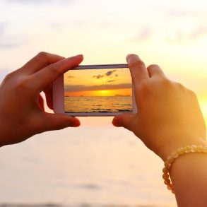 Woman hand using smartphone take a photo on the beach on Maui at sunrise