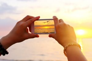 Woman hand using smartphone take a photo on the beach on Maui at sunrise