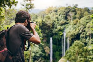 Male hiker photographing a west Maui waterfall in forest