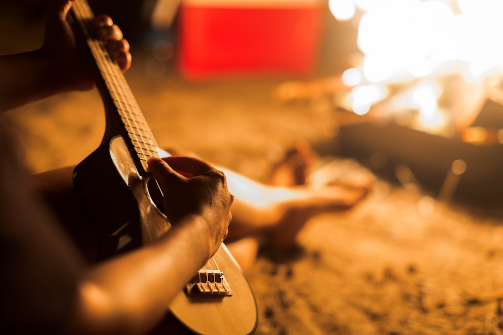 Man playing hawaiian guitar by campfire